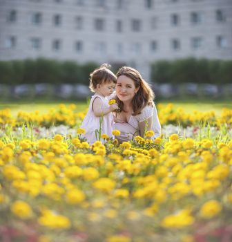 Happy mother sitting with daughter in yellow flowers meadow