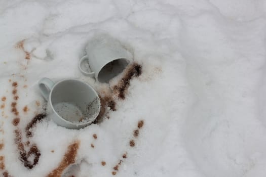 two white cups and the poured coffee in snow