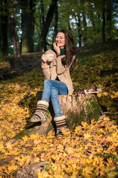 girl with a cup of coffee sitting on a tree stump in autumn Park