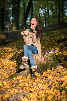 girl with a cup of coffee sitting on a tree stump in autumn Park