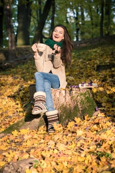 girl with a cup of coffee sitting on a tree stump in autumn Park