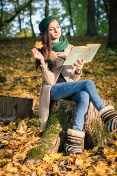 girl sits on the stump in the park, reading a book