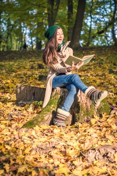 girl sits on the stump in the park, reading a book