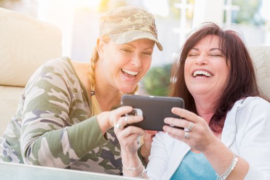 Two Female Friends Laugh While Using A Smart Phone on the Patio.