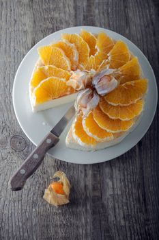 Cheesecake decorated with oranges and physalis on a table