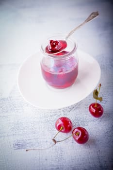 Jar of cherry jam and some cherries on the table