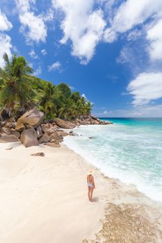 Woman wearing retro striped bikini and beach hat, enjoying amazing view on Anse Patates beach on La Digue Island, Seychelles. Summer vacations on picture perfect tropical beach concept.