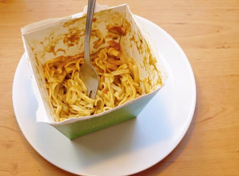 Leftover Thai noodles with green curry sauce and metal fork in paper box. Traditional noodles fast food. 