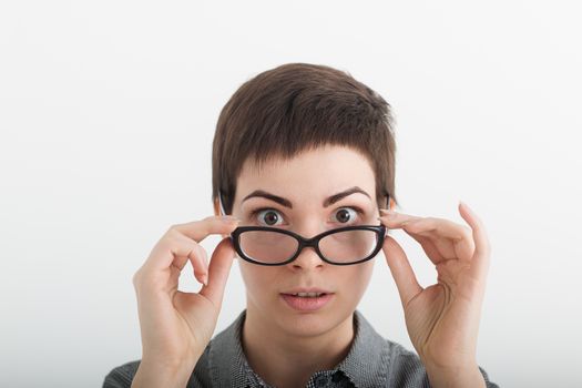 Close up of strict surprised young funny female teacher or student in glasses isolated on white background, looking over her glasses.