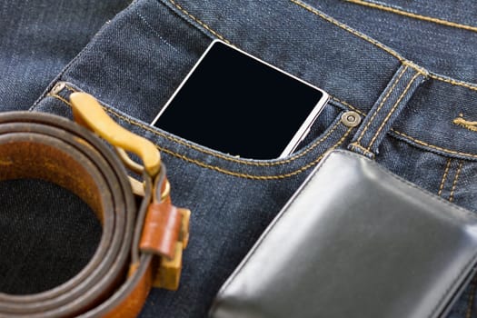 Top view of wallet and leather belt and smartphone on denim jeans pocket