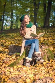 girl sitting on a stump and reads a book in the park