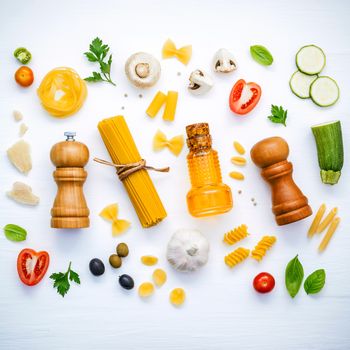 Italian food concept .Various kind of pasta with ingredients sweet basil ,tomato ,garlic ,parsley ,bay leaves ,pepper ,champignon,zucchini and parmesan cheese on white wooden background flat lay.