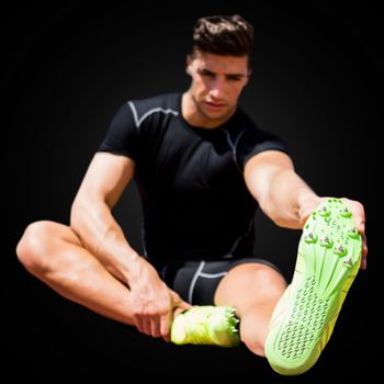Front view of sportsman is stretching his legs in a black background 