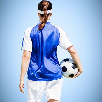 Rear view of woman soccer player holding a ball against blue background