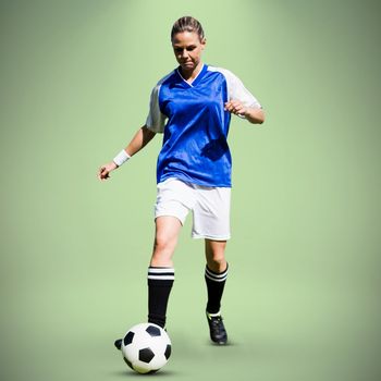 Woman soccer player progressing with a ball against green background