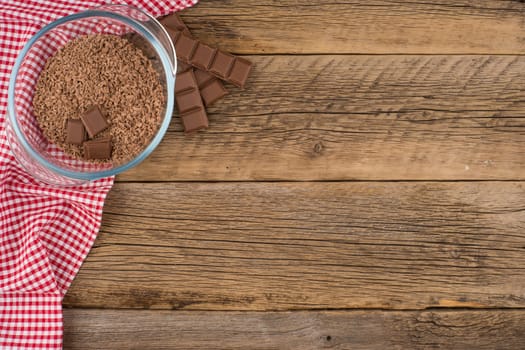 Grated chocolate in a glass bowl on the old wooden table. Top view.