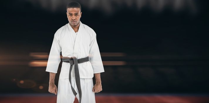 Portrait of serious karate player against composite image of playing field indoor