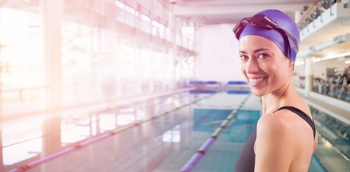 Fit swimmer standing by the pool smiling at camera at the leisure center