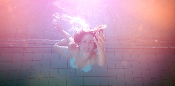 Pretty brunette smiling and offering her hand underwater in the swimming pool at the leisure centre