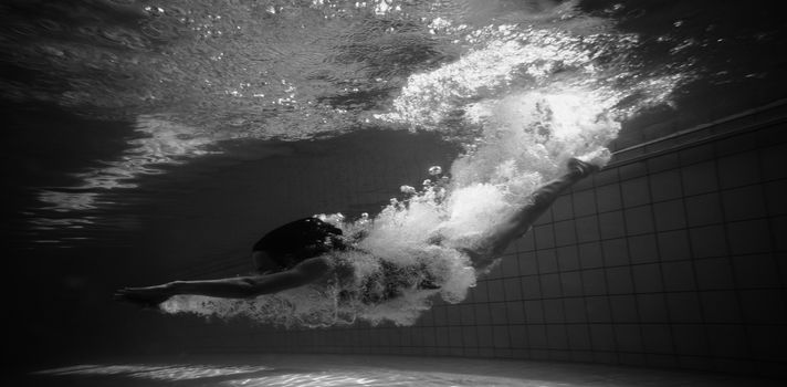 Athletic swimmer smiling at camera underwater in the swimming pool at the leisure centre