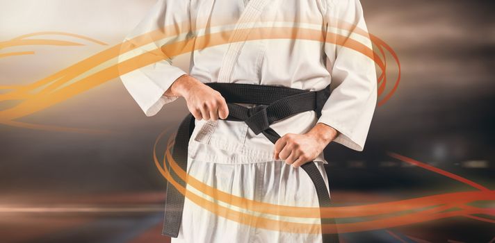 Mid section of fighter tightening karate belt against view of sport ground outdoor