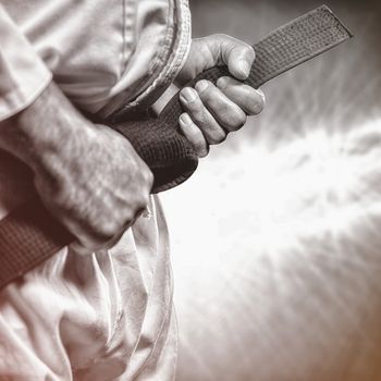 Fighter tightening karate belt against spotlights