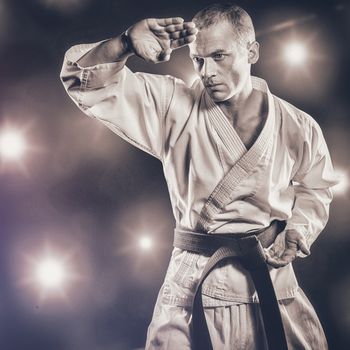 Fighter performing karate stance against composite image of orange spotlight 