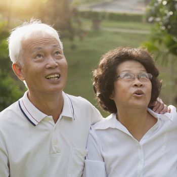 Portrait of healthy Asian seniors retiree couple looking up at outdoor nature park, morning beautiful sunlight background.