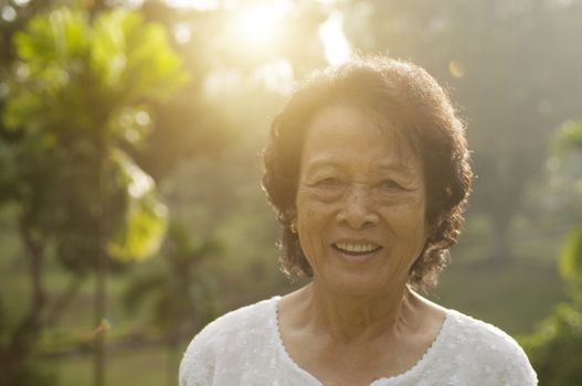 Portrait of healthy Asian senior woman smiling at outdoor nature park, morning beautiful sunlight background.