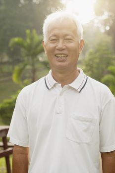 Portrait of healthy Asian senior man smiling at outdoor nature park, morning beautiful sunlight background.