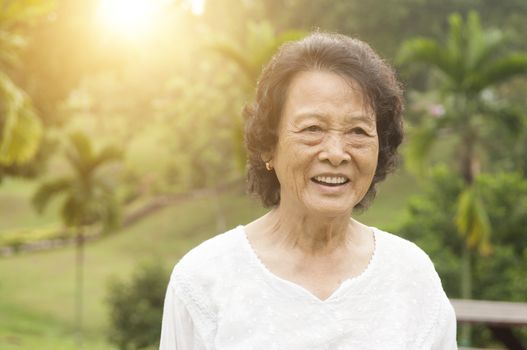 Portrait of healthy happy Asian senior woman smiling at outdoor nature park, morning beautiful sunlight background.