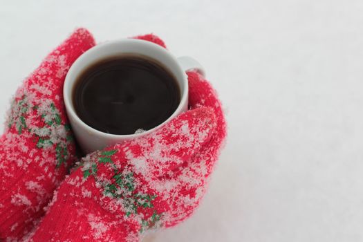 hands keep a cup of coffee against the background of snow in red gloves