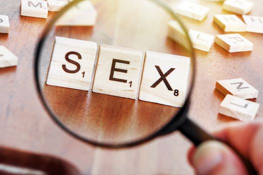 concept image of a magnifying glass zoom on a word SEX placed on a desk in precious wood