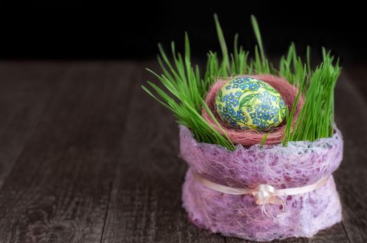 Decoupage Easter eggs and the germination of wheat in pot on wooden surface. Low key, selective focus.