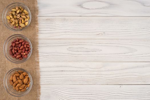 Mix nuts in a glass bowl on the old wooden table. Top view.