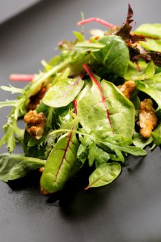 Fresh ecological salad mix with nuts on black plate, macro