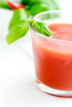 Cold tomato juice in a glass with basil leafs close up