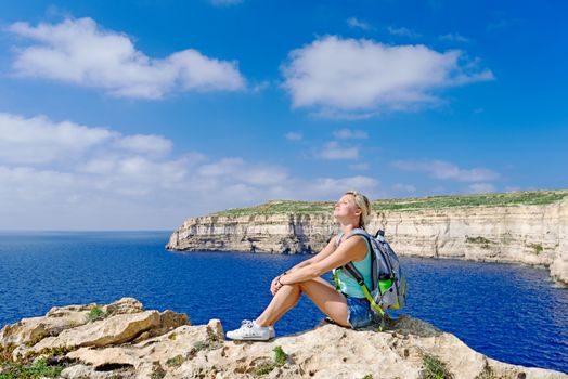 Girl enjoying sun on coast line near Azure Window on Gozo Island, Malta