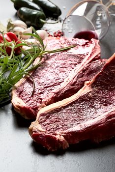 Raw aged meat T-bone steak and seasoning on dark background
