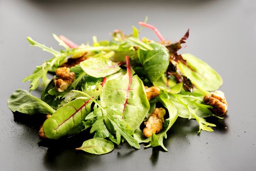 Fresh ecological salad mix with nuts on black plate, macro