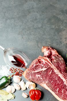 Raw aged meat T-bone steak and seasoning on dark background with copy paste
