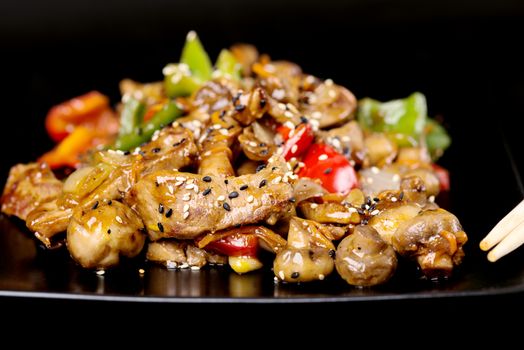 Black plate with meat and vegetables covered with sesame seeds