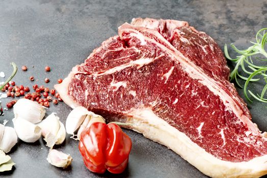 Raw aged meat T-bone steak and seasoning on dark background