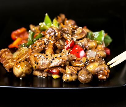 Black plate with meat and vegetables covered with sesame seeds