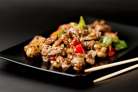 Black plate with meat and vegetables covered with sesame seeds