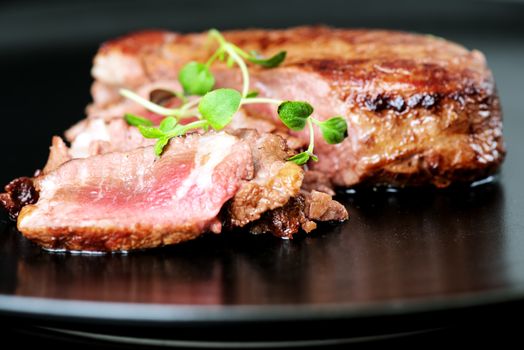 Delicious beef steak on a black plate, close-up