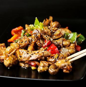 Black plate with meat and vegetables covered with sesame seeds