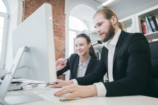 Two business people working together in the office looking at one monitor