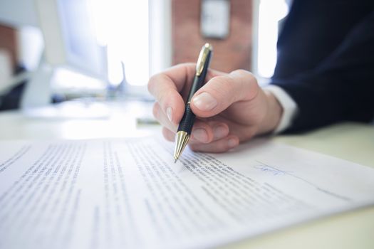 Businessman sitting at office desk signing a contract with shallow focus on signature and pen