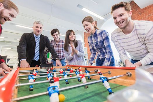 Employees playing table football indoor game in the office during break time